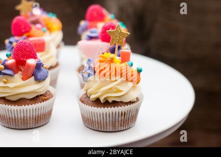 Schokoladencupcakes mit Frischkäse-Zuckerguss, pinka und Orangenkauen-Marmelade, Süßigkeiten und goldenem Topper auf dunklem Hintergrund Stockfoto