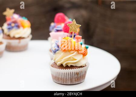 Schokoladencupcakes mit Frischkäse-Zuckerguss, pinka und Orangenkauen-Marmelade, Süßigkeiten und goldenem Topper auf dunklem Hintergrund Stockfoto