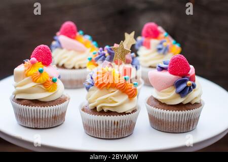 Schokoladencupcakes mit Frischkäse-Zuckerguss, pinka und Orangenkauen-Marmelade, Süßigkeiten und goldenem Topper auf dunklem Hintergrund Stockfoto