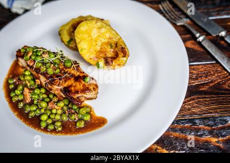 Gebratenes Kalbsfleisch mit Erbsenfleisch und Gratin-Kartoffeln auf Holztisch Stockfoto