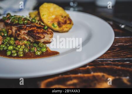 Gebratenes Kalbsfleisch mit Erbsenfleisch und Gratin-Kartoffeln auf Holztisch Stockfoto