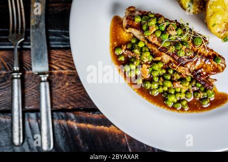 Gebratenes Kalbsfleisch mit Erbsenfleisch und Gratin-Kartoffeln auf Holztisch Stockfoto