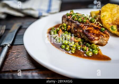 Gebratenes Kalbsfleisch mit Erbsenfleisch und Gratin-Kartoffeln auf Holztisch Stockfoto