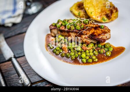 Gebratenes Kalbsfleisch mit Erbsenfleisch und Gratin-Kartoffeln auf Holztisch Stockfoto