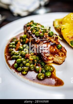 Gebratenes Kalbsfleisch mit Erbsenfleisch und Gratin-Kartoffeln auf Holztisch Stockfoto