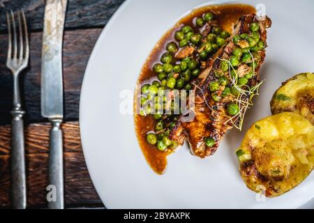 Gebratenes Kalbsfleisch mit Erbsenfleisch und Gratin-Kartoffeln auf Holztisch Stockfoto