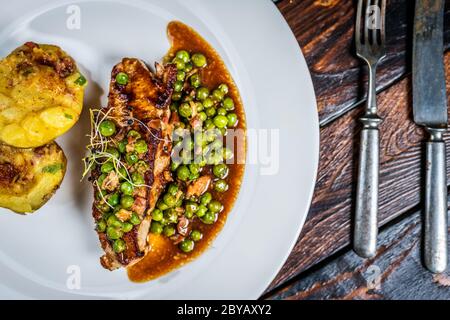 Gebratenes Kalbsfleisch mit Erbsenfleisch und Gratin-Kartoffeln auf Holztisch Stockfoto