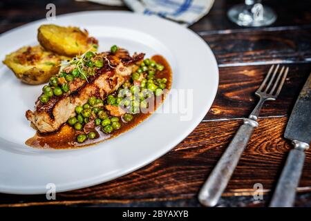 Gebratenes Kalbsfleisch mit Erbsenfleisch und Gratin-Kartoffeln auf Holztisch Stockfoto