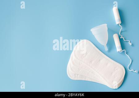 Sanitärpolster, Menstruationsbecher und Tampons auf blauem Hintergrund. Konzept der weiblichen Hygiene während der Menstruation. Stockfoto