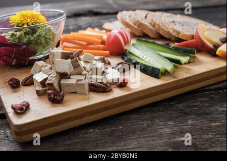 Low-Angle-Ansicht von veganen Snack oder Vorspeise mit frischem rohem Gemüse, Tofu-Würfel, Avocado-Aufstrich und Brot. Stockfoto