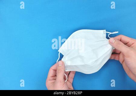 Hand mit einer weißen Gesichtsmaske in blauem Hintergrund. Draufsicht, flaches Lay mit Kopierfläche. Stockfoto