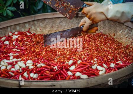 Chilis und Knoblauch werden von der Arbeiterinnen in einer Korbschale auf dem Straßenmarkt in Yangshuo, China, gehackt Stockfoto