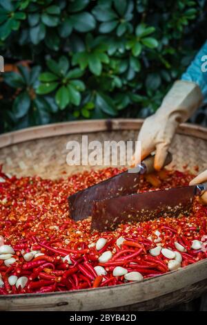 Chilis und Knoblauch werden von der Arbeiterinnen in einer Korbschale auf dem Straßenmarkt in Yangshuo, China, gehackt Stockfoto