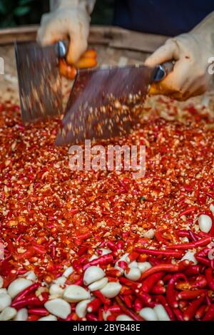Chilis und Knoblauch werden von der Arbeiterinnen in einer Korbschale auf dem Straßenmarkt in Yangshuo, China, gehackt Stockfoto