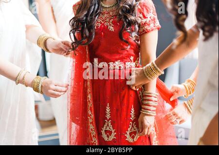 Bridemaids in weißen Sarees helfen indische Braut in rotem Kleid fertig zu machen Stockfoto