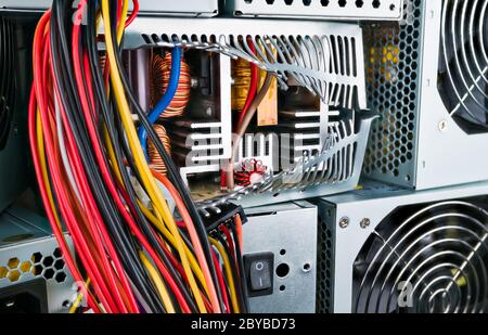 Netzteil im Inneren: Induktivitäten, Kühlkörper oder Transformator. Nahaufnahme des defekten Kästchens. Computerteil im Stapel der verwendeten Hardware. Farbige Kabel hängen. Stockfoto
