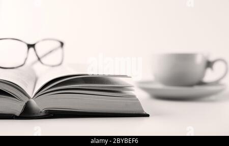 Offenes Buch, Tasse Tee Kaffee im weichen Fokus und Lesebrille auf weißem Hintergrund. Bleiben Sie zu Hause, freiberuflich, lernen von zu Hause Konzept Stockfoto