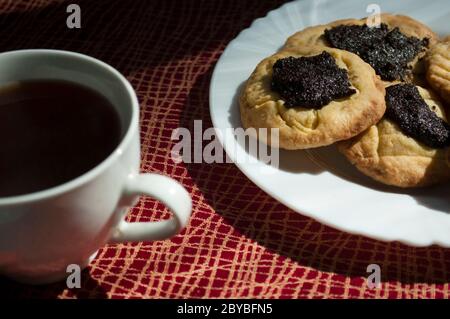 Gebissen Kekse mit Mohnfüllung und Kaffee auf Kastanientischdecke bei Tageslicht, Backstube Hintergrund, Food-Fotografie Stockfoto