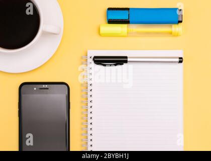 Planer Nahaufnahme Foto in der Draufsicht leeres Notebook, Bürozubehör, Handy und Tasse schwarzen Kaffee auf gelbem Hintergrund Stockfoto