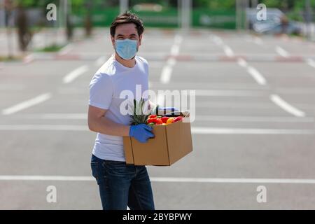 Portrait eines hübschen jungen Kuriers in Schutzmaske und medizinischen Handschuhen liefert Essen zum Mitnehmen. Lieferservice unter Quarantäne, Krankheit o Stockfoto