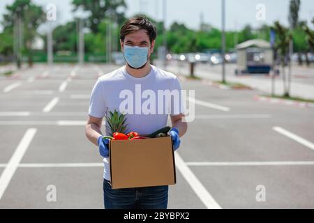 Portrait eines hübschen jungen Kuriers mit medizinischen Handschuhen und Maske liefert Essen zum Mitnehmen. Lieferdienst unter Quarantäne, Krankheitsausbruch, Stockfoto