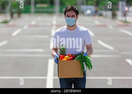Junger Kurier mit Schutzmaske und medizinischen Handschuhen liefert Essen zum Mitnehmen. Lieferservice unter Quarantäne, Krankheitsausbruch, Coronavir Stockfoto