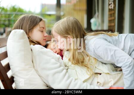 Zwei große Schwestern bewundern ihren neugeborenen Bruder. Zwei junge Mädchen halten ihren neuen Jungen. Kinder mit großem Altersunterschied. Großer Altersunterschied zwischen den beiden Stockfoto