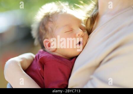 Niedliche kleine neugeborene Baby Junge in seiner Mutter Arme. Porträt von kleinen neuen Baby zu Hause. Liebenswert Sohn von seiner Mama gehalten. Neues Bündel Freude. Stockfoto