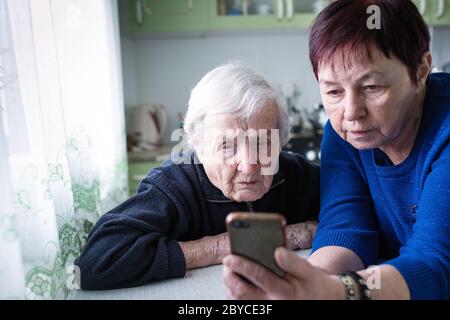 Eine Erwachsene Frau zeigt ihrer alten Mutter einen Smartphone-Bildschirm. Stockfoto