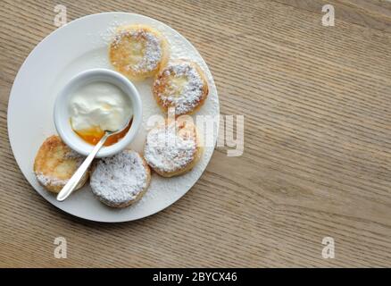 Flache Ansicht von fettfreien Käsekuchen aus Quark mit Honig und saurer Sahne bedeckt mit Puderzucker auf weißem Teller Stockfoto
