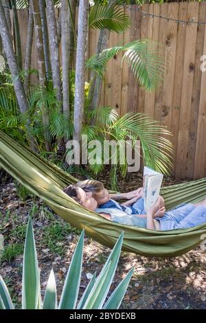 Eine Mutter liest ihrem kleinen Jungen ein Buch, während sie zusammen in einer Hängematte in ihrem Hinterhof in Miami, Florida liegen. Stockfoto