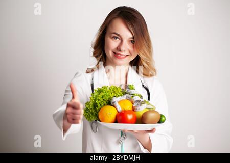 Eine junge Ernährungsberaterin hält in den Händen frisches Gemüse und Obst auf dem Teller im Sprechzimmer Stockfoto