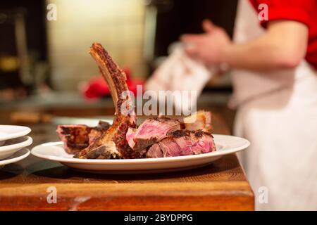 Saftiges mittelgroßes Rindfleisch Rib Eye Steak Scheiben auf weißem Teller, bereit zum Servieben, Koch im Hintergrund in einem Küchenrestaurant Stockfoto