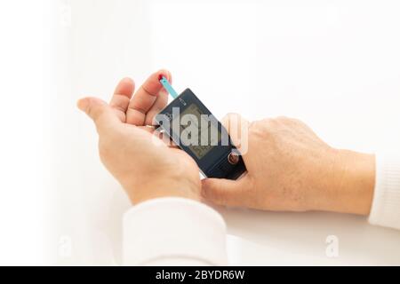 Hände einer Person, Frau oder Mann, die sich selbst überprüft, sein Diabetes- und Blutzuckermessgerät mit digitalem Manometer, Glucometer. Gesundheitswesen und Medi Stockfoto
