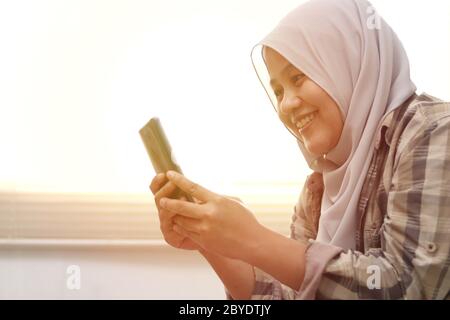 Nahaufnahme einer asiatischen muslimischen Frau mit einem Smartphone. Fröhliche lächelnde Geste gute Nachrichten bei der Kommunikation im Internet online, Videoanruf Stockfoto