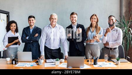 Lächelnde Mitarbeiter, Die In Der Nähe Des Tisches Im Modernen Büro, Panorama Stehen Stockfoto