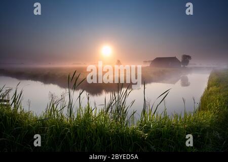 Nebliger Sonnenaufgang über dem Fluss in Ackerland Stockfoto