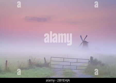 Holländische Windmühle im dichten Nebel bei Sonnenaufgang Stockfoto