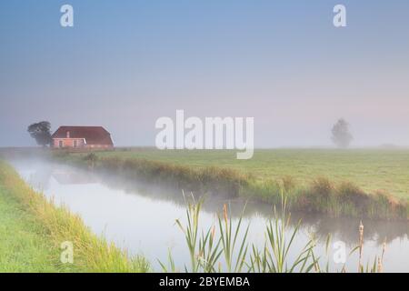 Bauernhaus am Flussufer im Morgennebel Stockfoto