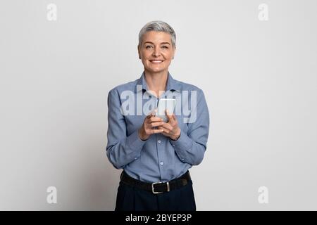 Geschäftsanwendung Lächelnd Reife Weibliche Unternehmer Holding Smartphone Und Lächelnd An Kamera Stockfoto
