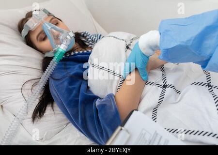 Überprüft den Blutpuls. Infektiöser Stationsarzt. Ein junger Teenager liegt in einem Krankenhausbett. Stockfoto