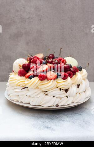 Großer Pavlova-Baiser mit frischen Beeren und Makronen auf schlichtem grauen Hintergrund. Speicherplatz kopieren. Stockfoto