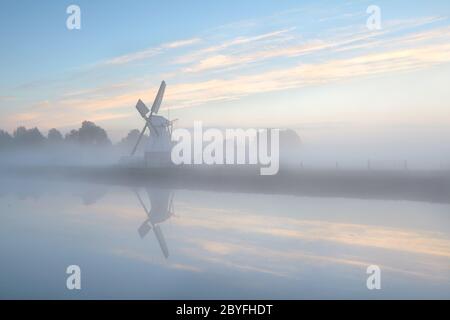 Holländische Windmühle im dichten Nebel während Sonnenaufgang Stockfoto