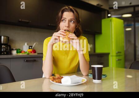 Dunkelhaarige Mädchen beißen einen Burger Blick auf die Seite Stockfoto