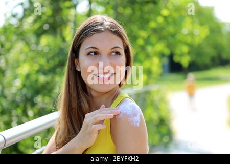 Lächelnde junge Frau, die Sonnenschutz auf der Schulterhaut im Freien an einem Sommertag, Blick zur Seite. Kopierbereich. Stockfoto