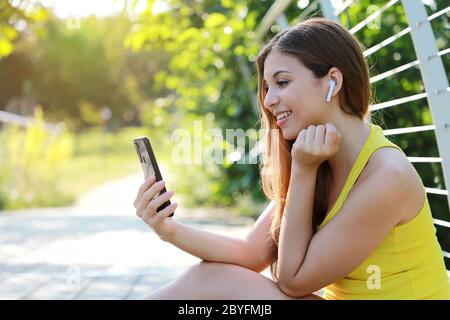 Liebenswert sportliche Mädchen sitzt im Park genießen Musik hören mit Handy-App mit drahtlosen Kopfhörer bei Sonnenuntergang Stockfoto