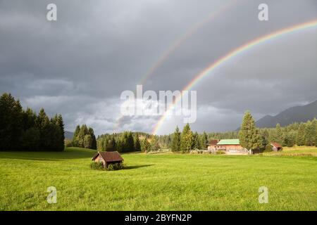 Farbenfroher Regenbogen bei Regen in den Alpen Stockfoto