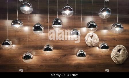 Viele runde Lampen in der Nähe einer braunen Holzwand. Runde Lichter im Innenraum. Hintergrund für Design. Dekorative Glühlampen Stockfoto