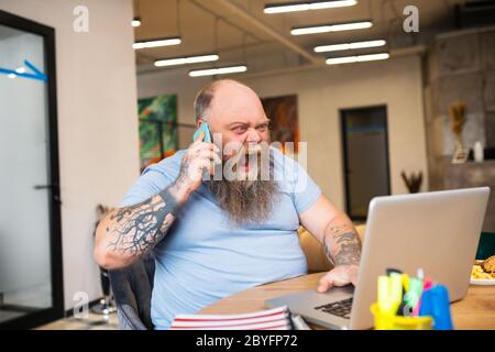 Kahlköpfiger Mann, der am Telefon redet und wütend aussieht Stockfoto
