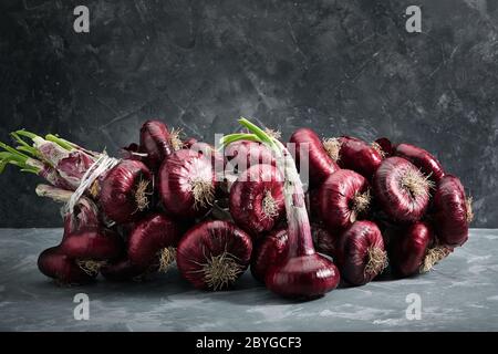 Rote Zwiebeln auf grauem Hintergrund, frisches Bio-Gemüse. Küche und Kochkonzept. Zutat für Salate, Suppen, Gerichte. Stockfoto